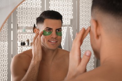 Photo of Man applying green under eye patch near mirror at home