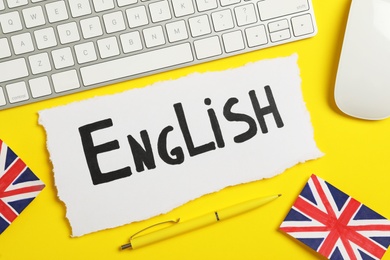 Photo of Paper with word English, keyboard, mouse and UK flags on yellow background, flat lay