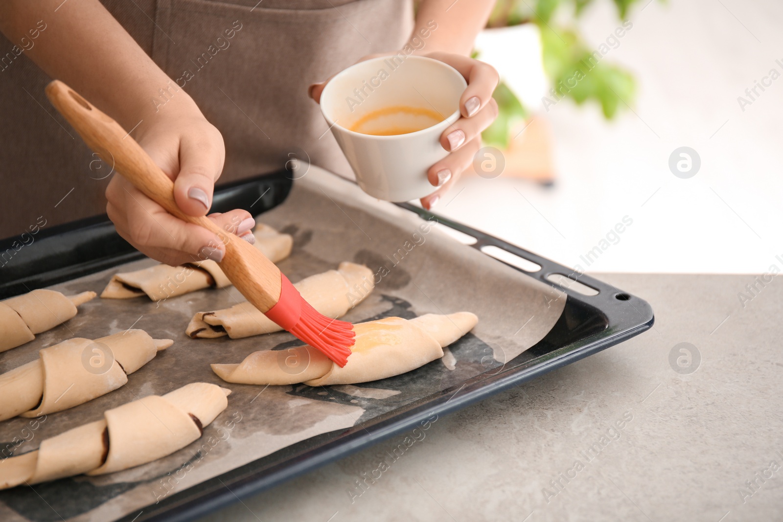 Photo of Woman spreading egg yolk on croissants, closeup