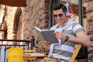 Photo of Handsome man reading book in outdoor cafe