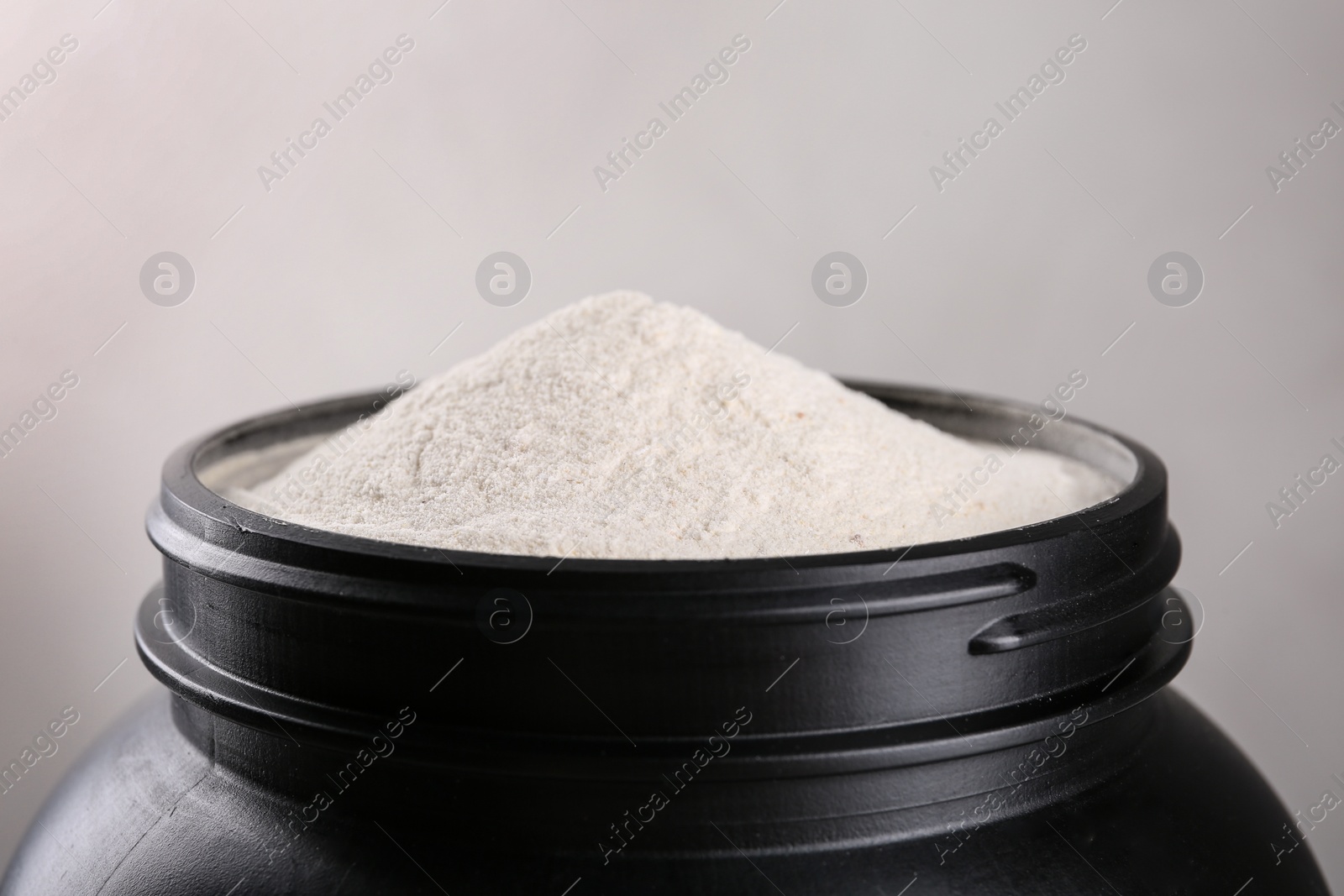 Photo of Black jar full of protein powder on light background, closeup