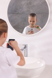 Photo of Little girl using smartphone while brushing teeth in bathroom, space for text. Internet addiction