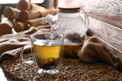 Wicker mat with freshly brewed tea near wooden wall in room. Cozy home atmosphere