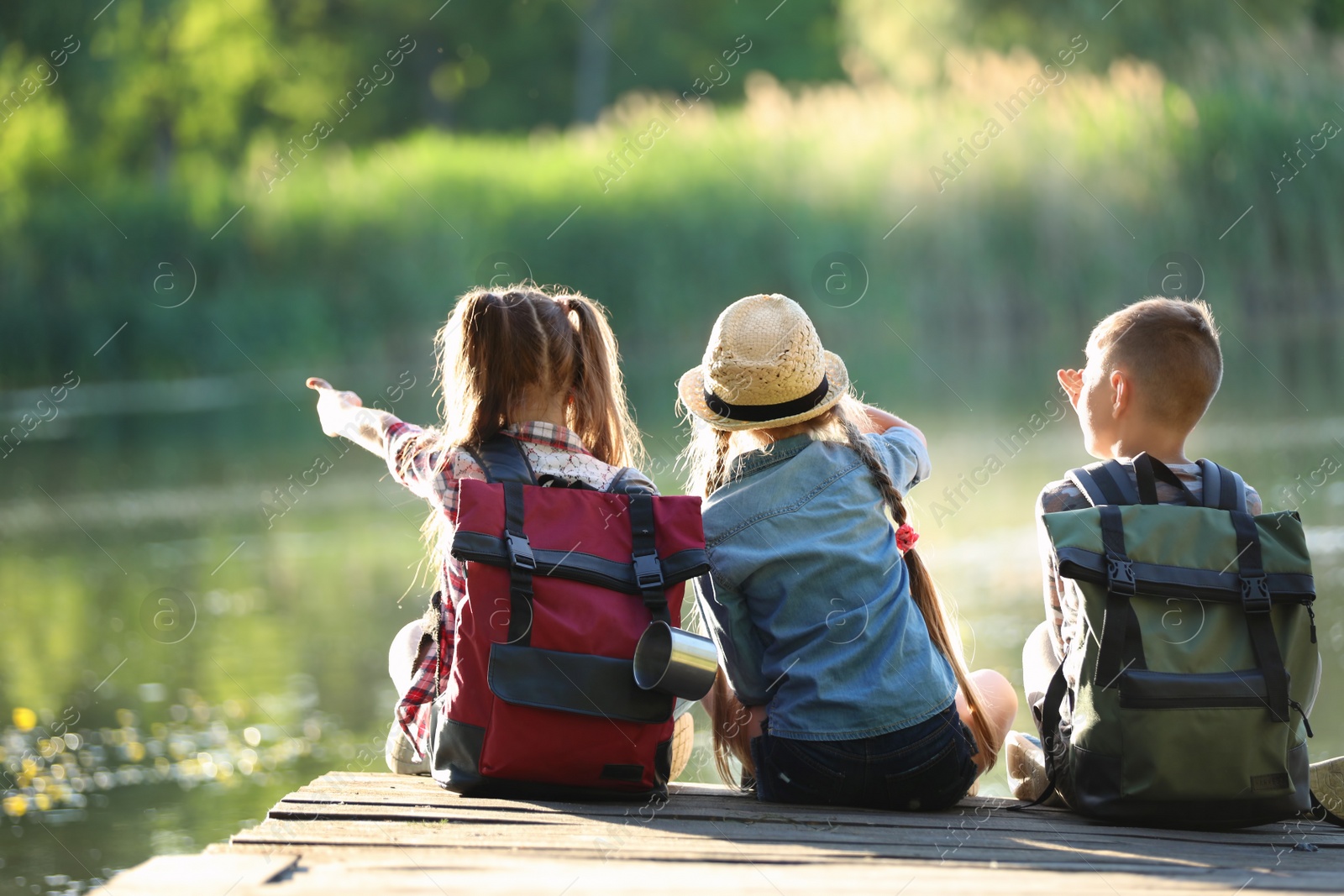 Photo of Little children sitting on wooden pier. Summer camp