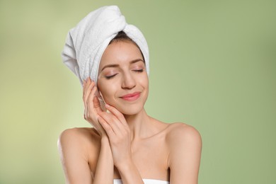 Photo of Beautiful young woman with hair wrapped in towel after washing on light green background