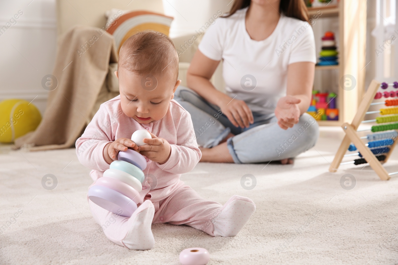 Photo of Cute baby girl playing with toy pyramid and mother on floor at home