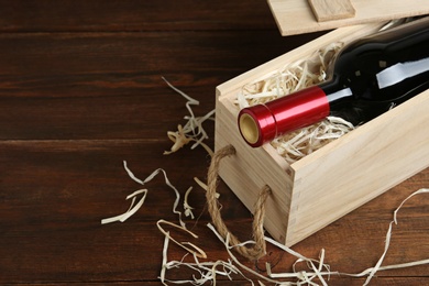 Photo of Open wooden crate with bottle of wine on table, space for text