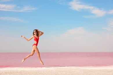 Beautiful woman in swimsuit jumping near pink lake on sunny day