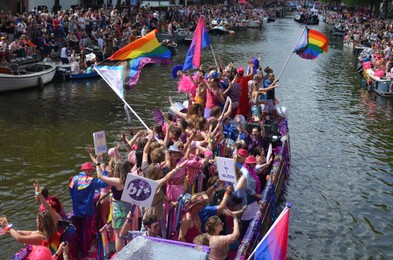 Photo of AMSTERDAM, NETHERLANDS - AUGUST 06, 2022: Many people in boats at LGBT pride parade on river