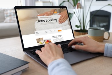 Image of Woman using laptop to book hotel at wooden table, closeup