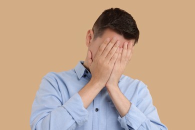 Resentful man covering face with hands on beige background