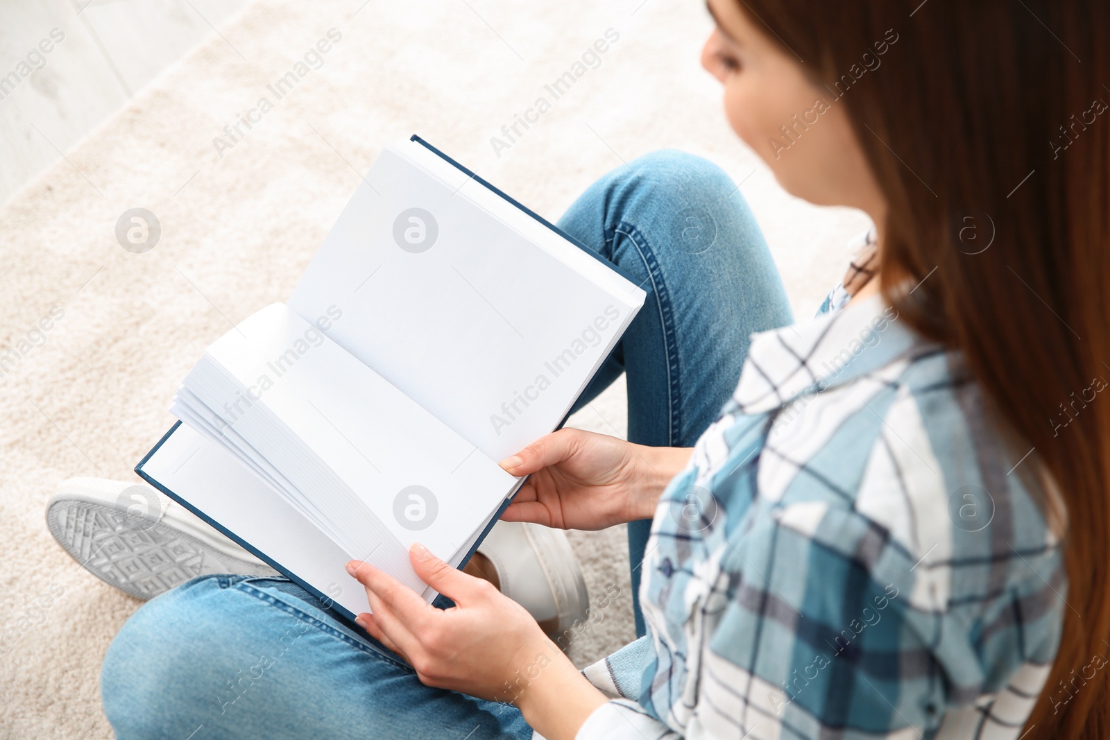 Photo of Beautiful young woman reading book on floor at home