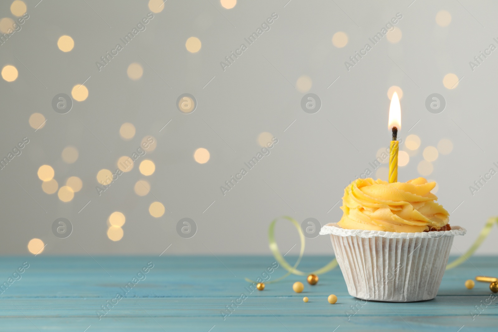 Photo of Tasty birthday cupcake on light blue wooden table against blurred lights. Space for text