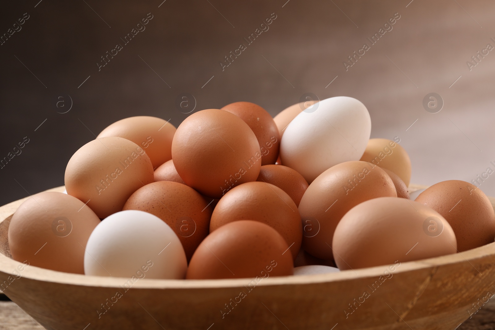 Photo of Fresh chicken eggs in bowl on light brown background, closeup