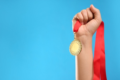 Woman holding gold medal on light blue background, closeup. Space for text