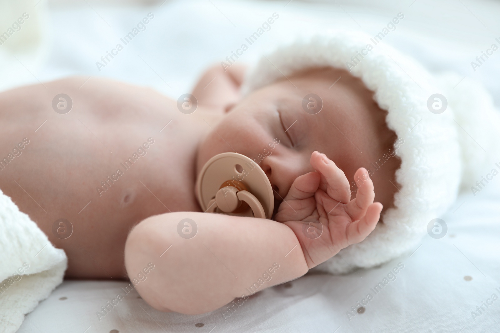 Photo of Cute newborn baby in white knitted hat sleeping on bed, closeup