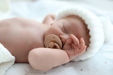 Photo of Cute newborn baby in white knitted hat sleeping on bed, closeup