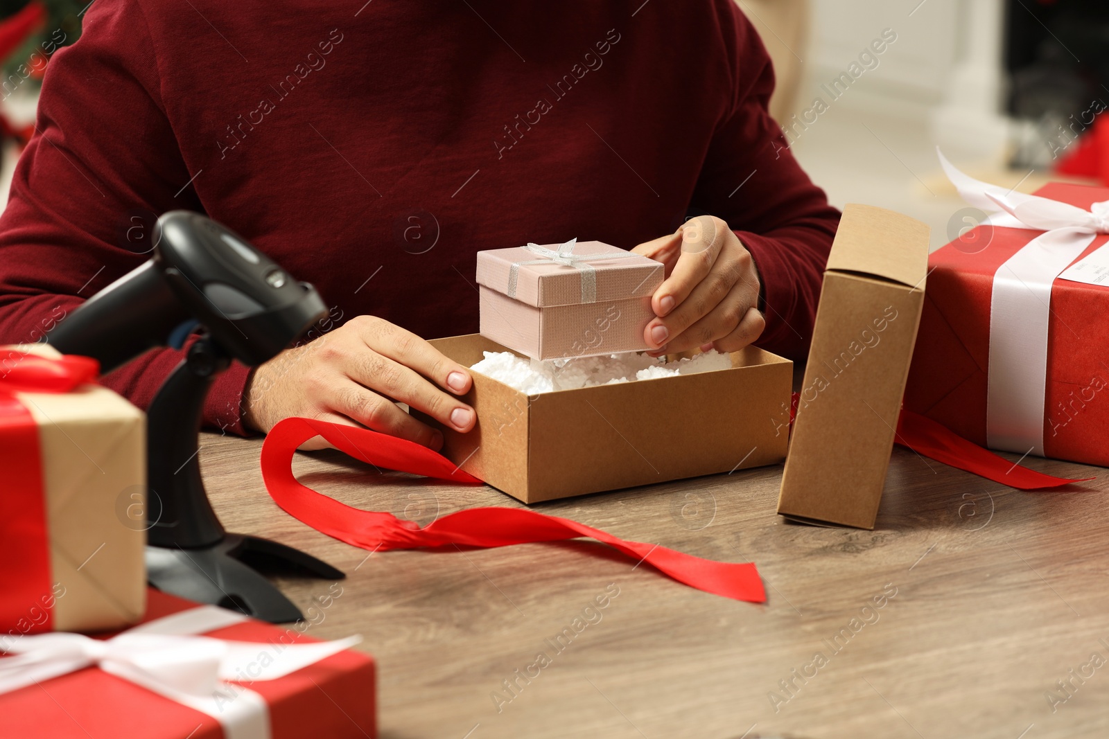 Photo of Man putting Christmas gift box into parcel at wooden table in post office, closeup