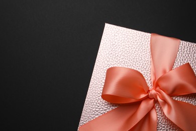Photo of Gift box with satin ribbon and bow on black background, top view. Space for text