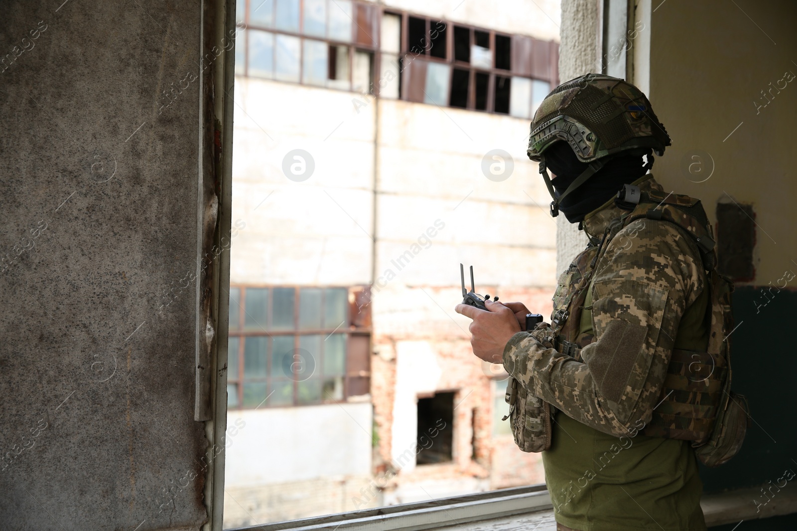 Photo of Military mission. Soldier in uniform with drone controller inside abandoned building, space for text