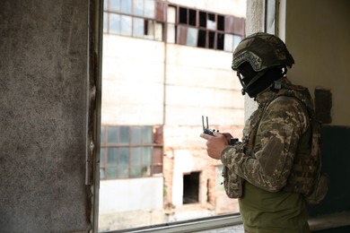 Military mission. Soldier in uniform with drone controller inside abandoned building, space for text