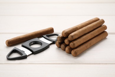 Photo of Many cigars and guillotine cutter on white wooden table