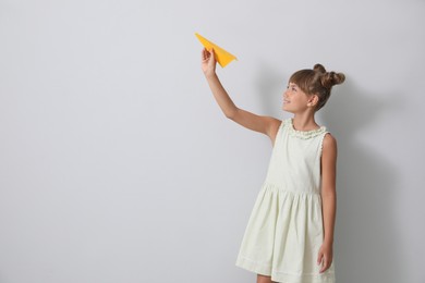Photo of Cute little girl playing with paper plane on light grey background. Space for text