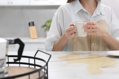 Photo of Woman with spilled coffee over her shirt at marble table in kitchen, closeup