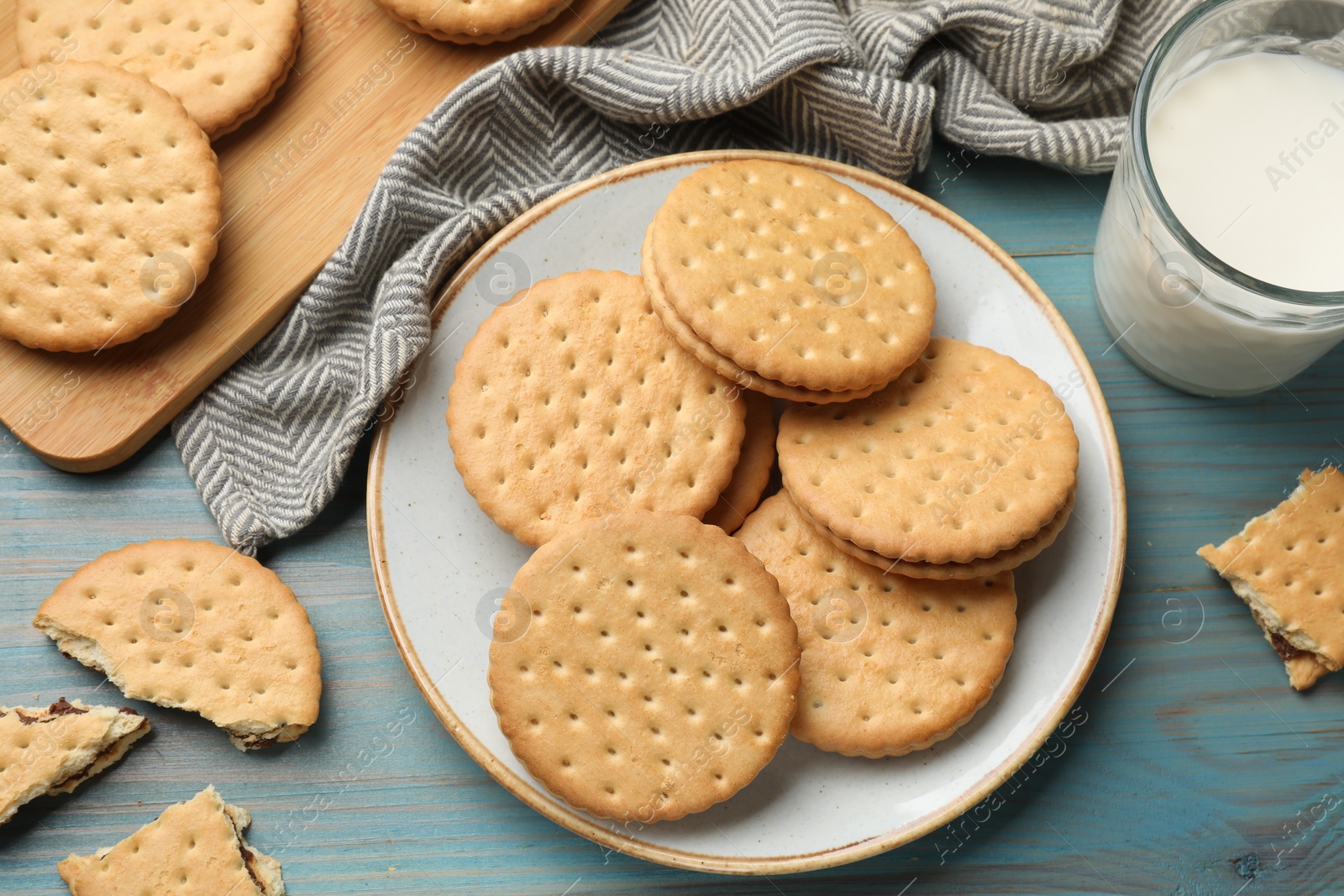 Photo of Tasty sandwich cookies and glass of milk on light blue wooden table, flat lay