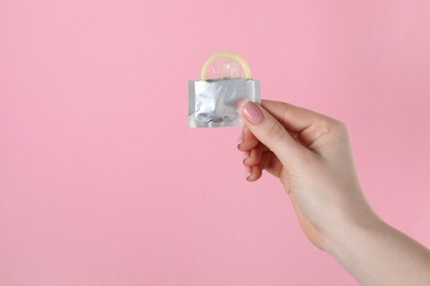 Woman holding condom on pink background, closeup. Space for text