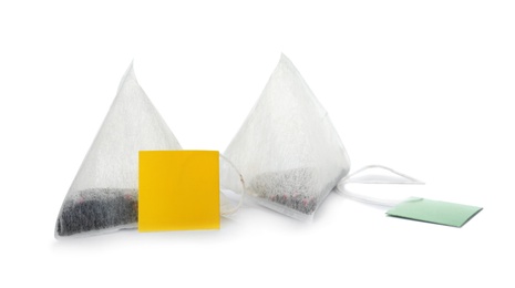 Photo of Unused pyramid tea bags with tags on white background. Space for text