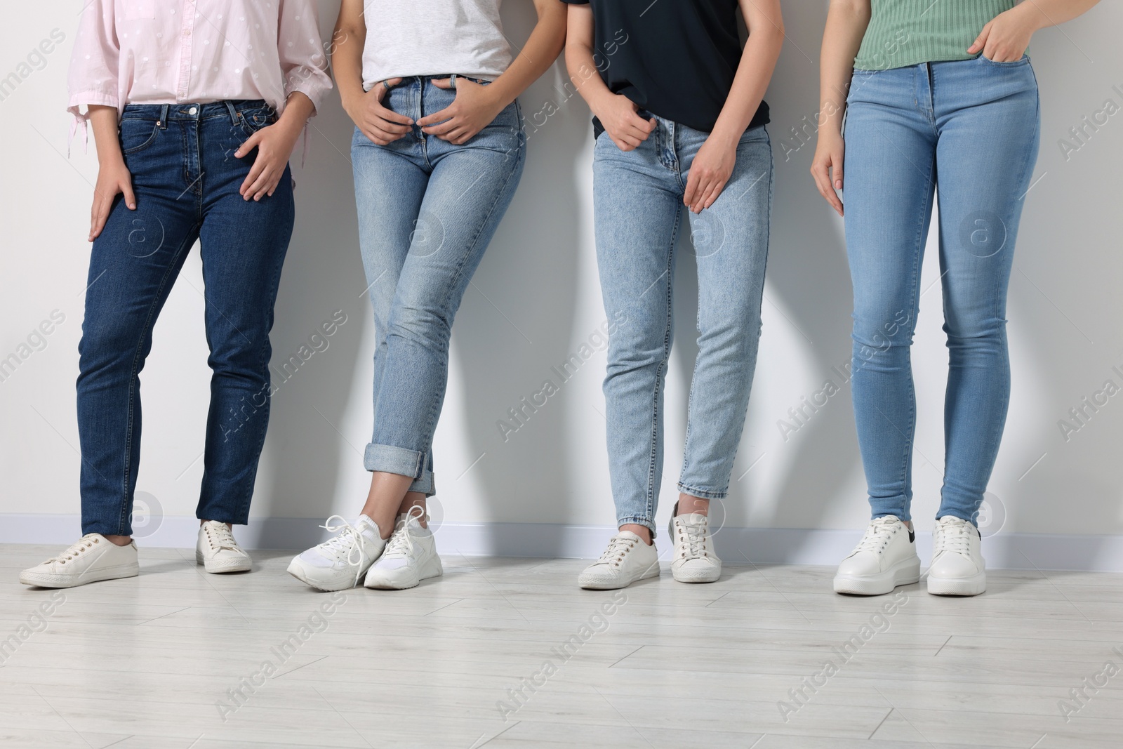 Photo of Women in stylish jeans near white wall, closeup