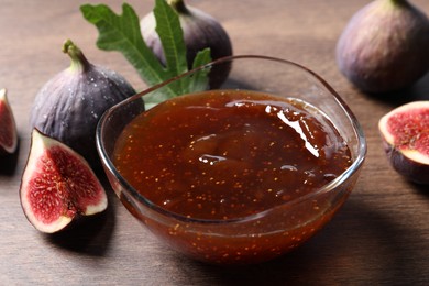 Photo of Glass bowl with tasty sweet jam and fresh figs on wooden table, closeup