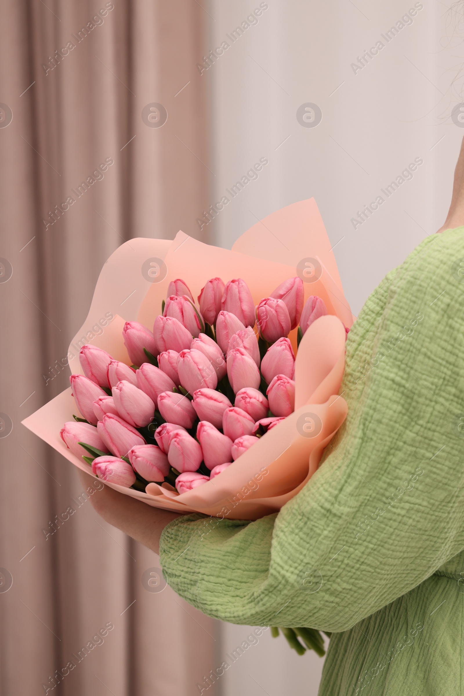 Photo of Woman holding bouquet of pink tulips indoors, closeup