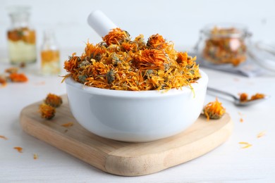 Photo of Mortar of dry calendula flowers on white table