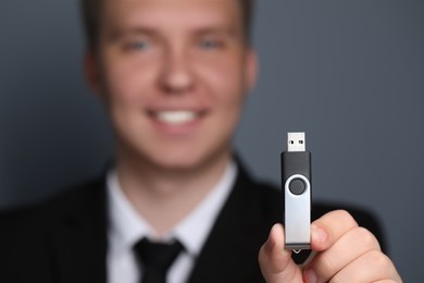 Photo of Man with usb flash drive against grey background, focus on device. Space for text