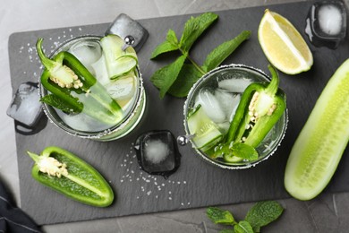 Spicy cocktail with jalapeno, cucumber and lime on black table, flat lay
