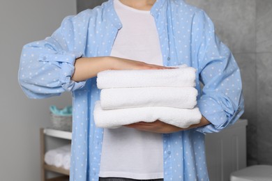 Photo of Woman holding folded soft terry towels in bathroom, closeup