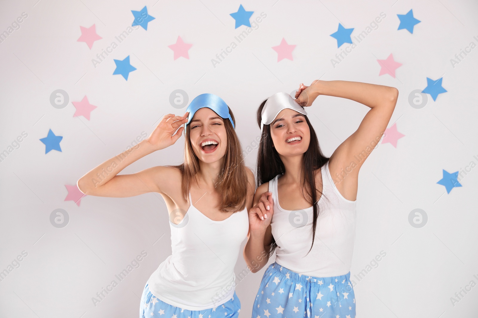 Photo of Beautiful women wearing sleeping masks on light grey background. Bedtime