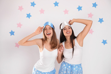 Beautiful women wearing sleeping masks on light grey background. Bedtime