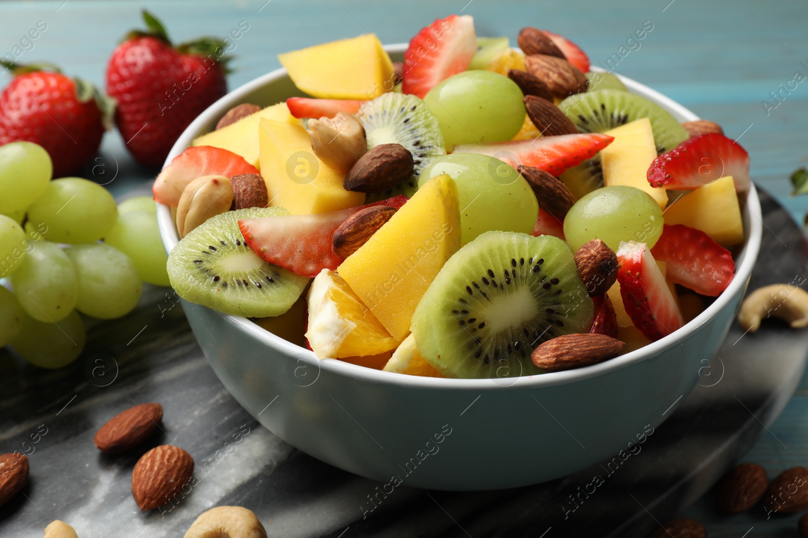 Photo of Tasty fruit salad in bowl and ingredients on table, closeup