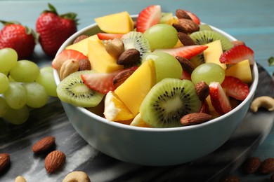 Tasty fruit salad in bowl and ingredients on table, closeup