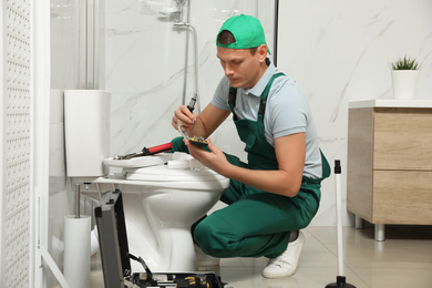 Photo of Professional plumber repairing toilet tank in bathroom