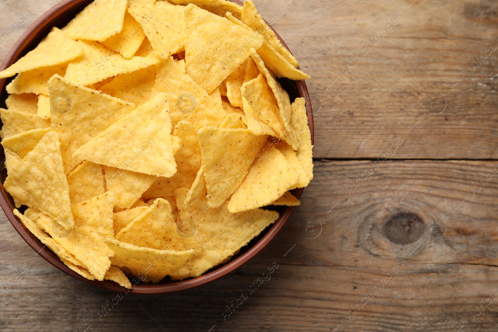 Photo of Bowl with tasty tortilla chips (nachos) on wooden table, top view. Space for text