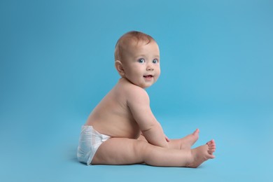 Photo of Cute baby in dry soft diaper sitting on light blue background
