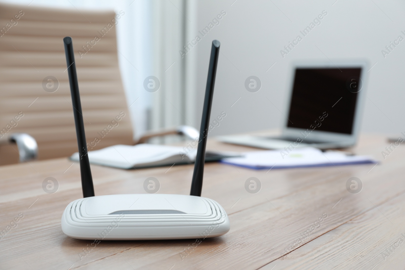 Photo of Modern Wi-Fi router on wooden table with laptop indoors