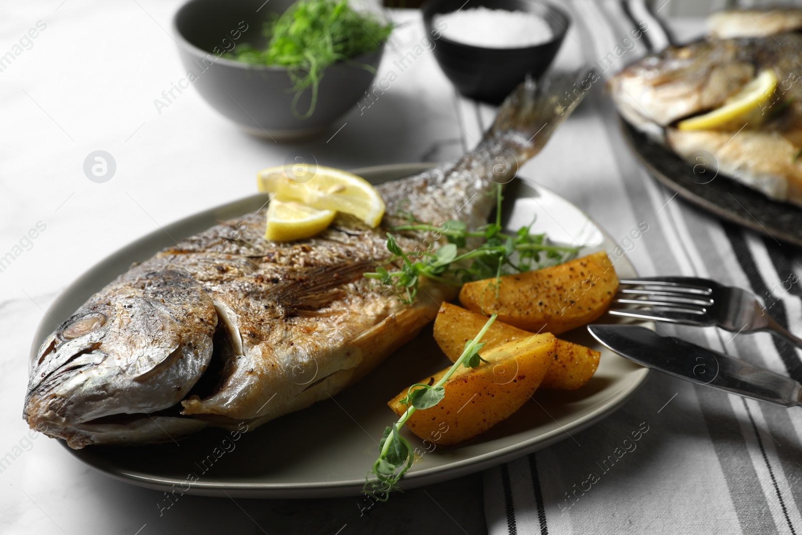 Photo of Seafood. Delicious baked fish served with lemon, potato and microgreens on light table, closeup