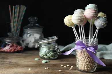 Photo of Sweet cake pops on wooden table against black background. Space for text