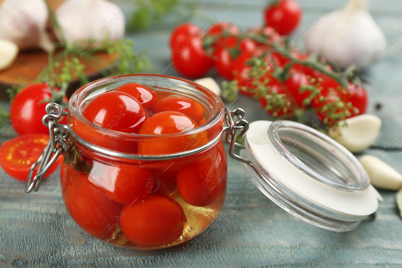 Photo of Glass jar of pickled cherry tomatoes on light blue wooden table, closeup