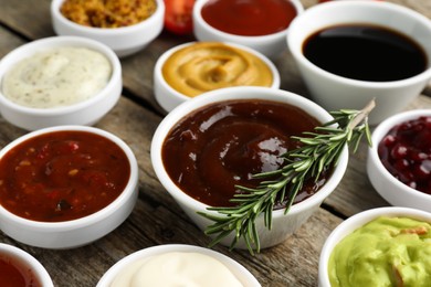 Photo of Different tasty sauces in bowls and rosemary on wooden table, closeup